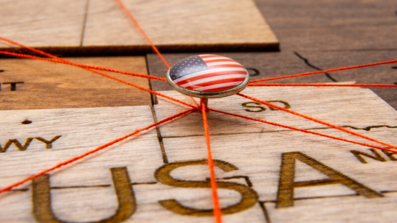 USA flag on the pushpin and red threads on the wooden map. Travel or logistic routes. Influence in geopolitics and world economy.